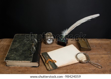 Quill ink pen and inkwell, antique book, magnifying glass, old notepad, vintage spectacles, clock on wood table