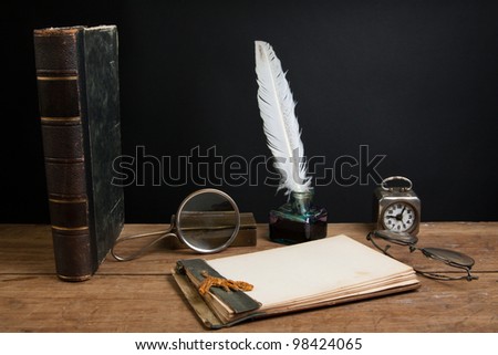 Antique book, quill ink pen and inkwell, magnifying glass, old notepad, vintage clock, spectacles on wood table