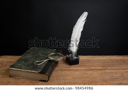 Quill ink pen and inkwell, old book and magnifying glass on wood table