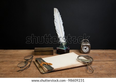 Old notepad, quill ink pen and inkwell, magnifying glass, vintage clock, spectacles on wood table