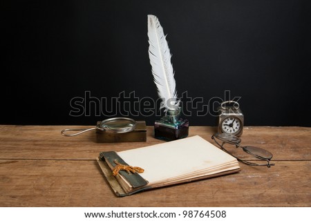 Old notepad, quill ink pen and inkwell, magnifying glass, book, vintage clock, spectacles on wood table