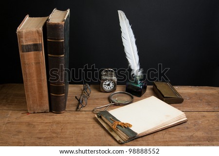 Quill ink pen and inkwell, antique books, magnifying glass, old notepad, vintage clock, spectacles on wood table