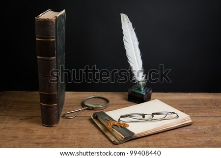 Notepad, quill ink pen and inkwell, magnifying glass, book, spectacles on wooden table