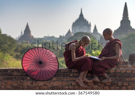 Couple of novice read a book on monastery\'s wall with field of ancient pagoda background in Old Bagan Myanmar