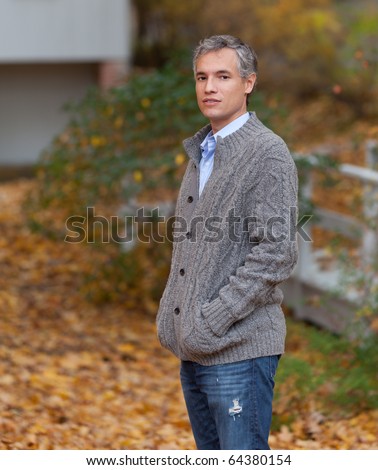 A handsome man with gray hair poses in front of a beautiful colorful fall / autumn background
