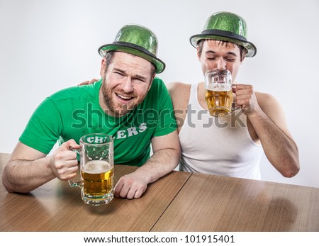 Male friends drinking on Saint Patrick\'s Day from large mugs of lager in green hats, wife beater, shirt, at favorite tavern having a good time