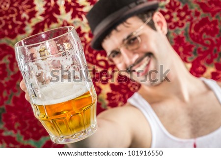 Smiling man at retro vintage bar with mostly empty mug of yellow beer toasting you, breaking fourth wall, in glasses hat and mustache, wife beater