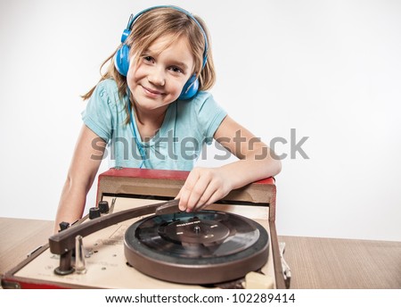 Young blonde girl smiling at music on vintage record player tunes LP with blue headphones shirt