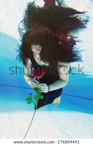 Beautiful young Asian woman in a black dress with long black hair under the water holding a red rose in her hand