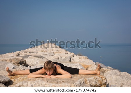 Beautiful young woman in Hanuman posture practicing yoga on the beach on the rocks