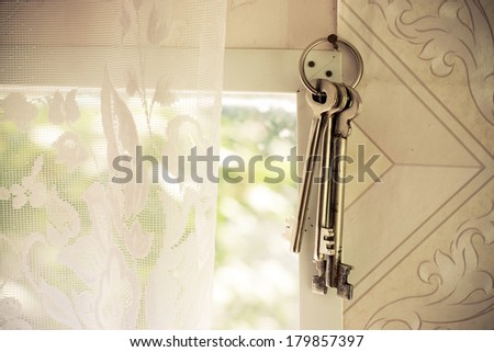 A set of old jail keys on a hoop hanging on a metal hook on a wall near the window
