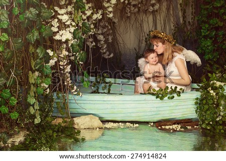 Mother holding and kissing the baby in a boat on the pond. Fairy picture angels with wings