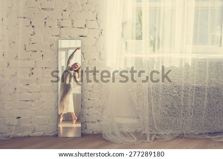 Beautiful dancing woman in white dress in the bright interior. Reflection in the mirror