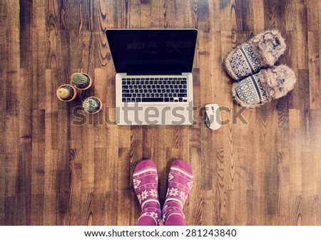 Woman feet in warm socks standing on a wooden floor with a laptop in winter. Online work concept