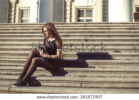 Young student girl sitting outdoor on the steps of University with tablet in hands