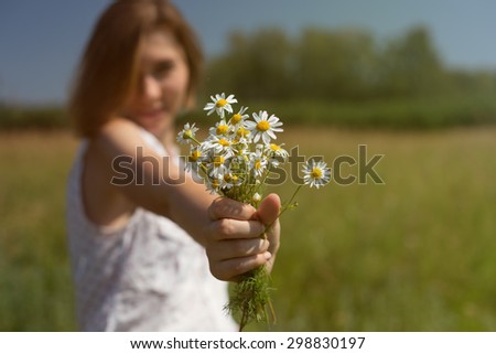 Young Happy Woman gives Flowers chamomile in sunny meadow