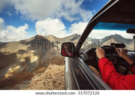Driver in car on the edge of cliff in wild mountains