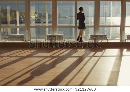 Woman standing near large window and looking to sunset. Big window, glass wall, warm room, sun and sea