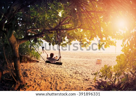 Happy boy kid on swing enjoy freedom and summer on sea shore on sunset