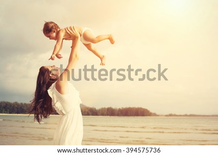Happy loving mother and her baby child playing outdoors on the sea beach