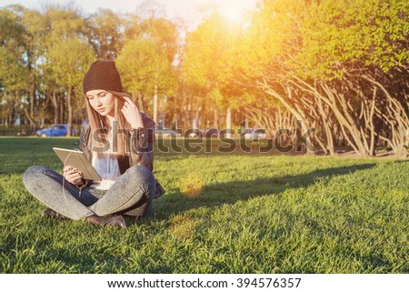 Young Student Woman Hipster Style sitting outdoor with tablet pc, listening music and communicate with friends through social network