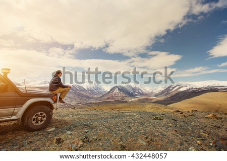 Young man sitting on his car in beautiful mountains landscape. Off-road travel vacation, enjoy  freedom