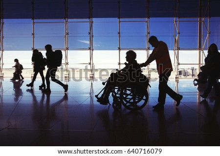 Silhouette of  man in wheelchair and people carrying luggage and walking in  airport