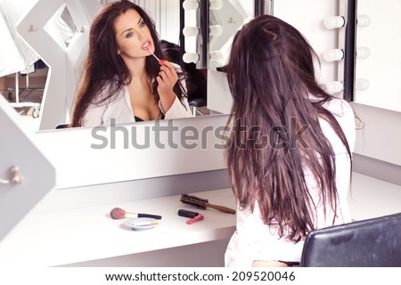 Sexy brunette in white shirt sitting on the visage's by the mirror putting makeup on