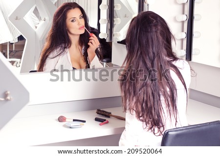 Young sexy brunette in white blouse, sitting on the visage\'s chair, looking in the mirror