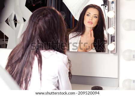 Young sexy brunette in white blouse, sitting on the visage\'s chair, looking in the mirror