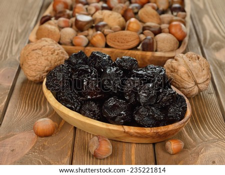 Dried prunes in a wooden bowl on a brown background