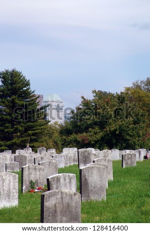Headstones in the foreground of a city building and an overcast sky.
