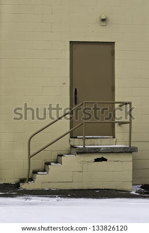 Behind a warehouse steps with railing leading to a brown door.
