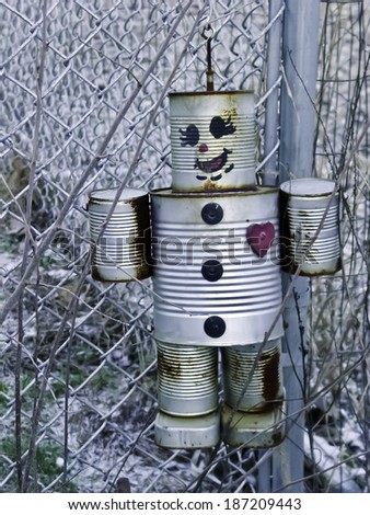 A model robot made of tin cans hanging on a fence as a scarecrow.