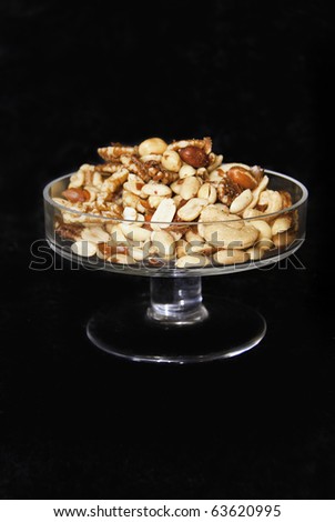 A clear glass dish full of mixed nuts on a black background.