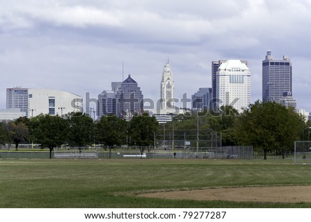 A view of a city scape as seen with a baseball field in the foreground and an overcast sky in the background.