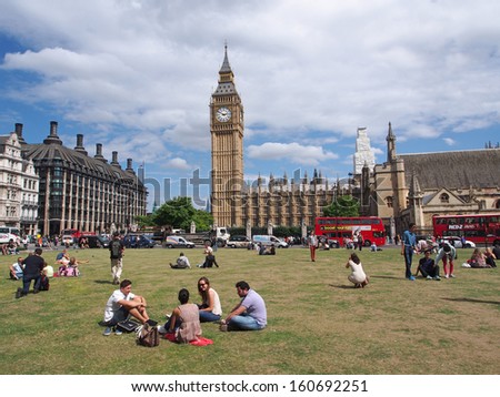 LONDON - AUGUST 5, 2013:  London\'s busy traffic moves around the Parliament Building as tourists rest in a quiet park across the street, in London on August 5, 2013.