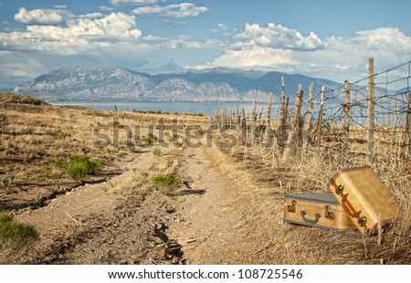 Vintage luggage sitting by a dirt road with mountains and lake