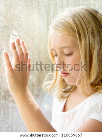 Child or teen looking down with hand on a rainy window