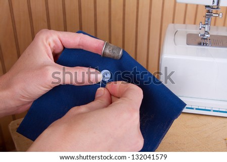 Sewing a button onto blue fabric with sewing machine in background