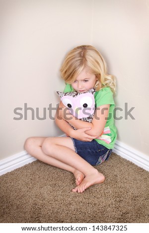 sad or lonely child in corner hugging a toy or stuffed animal