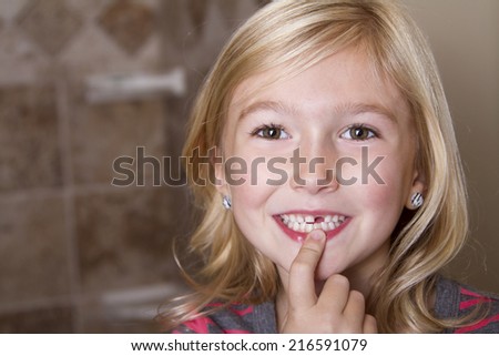 Child missing front tooth pointing at it with her finger
