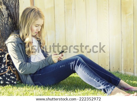 Teenage girl using a cell phone, texting, surfing the internet or playing a game, in an outdoor setting.