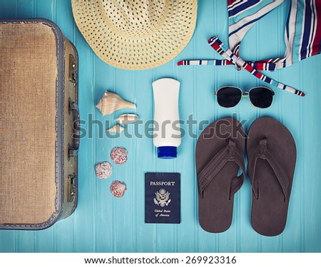 A collection of travel items including suitcase, passport, sandals, sunglasses, swim suit, sunscreen and straw hat on turquoise background