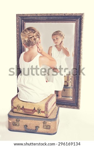 Child or young girl staring at herself in a mirror, sitting on vintage luggage, with a fish tail braid in her hair. Vintage or retro filter applied.