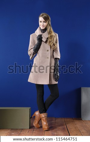 Full length young woman in coat posing with cube on wooden floor
