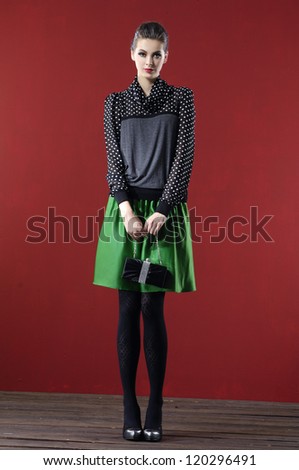 Full body young fashion model wearing elegant clothes holding bag posing wooden floor