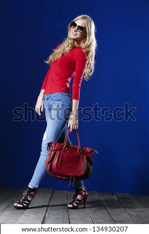 Full length portrait of young woman in sunglasses with bag posing wooden floor