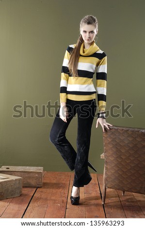 Full length young woman posing near chair with cube on wooden floor