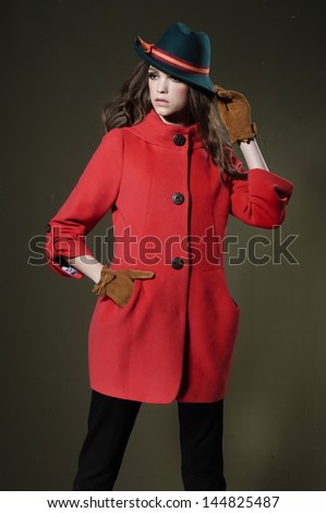 Portrait of fashion model woman in hat with red coat posing on dark background